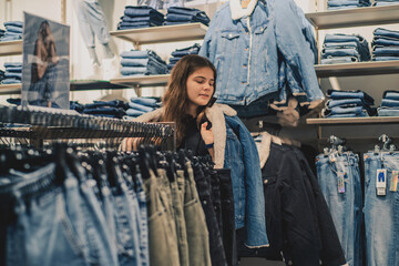 Smiling girl shopper choosing new jeans at store