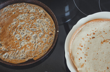 Baking pancakes in a frying pan close-up, ready-made pancakes on a plate.