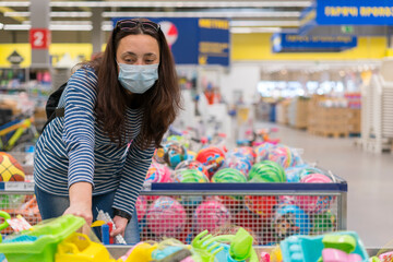 Woman in a protective mask in a supermarket chooses children's toys. Woman in medical mask at the...