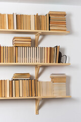 Light wooden bookshelves with hardback overturned books in white interior, home library