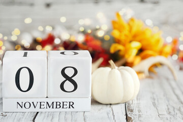 White wood calendar blocks with the date November 8th and autumn decorations over a wooden table. Selective focus with blurred background. 