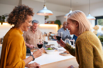 Group Of Mature Friends Meeting At Home Preparing Meal And Drinking Wine Together