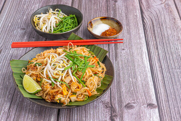 Pad Thai served with vegetables and lemon slice on banana leaves on a black plate on a wooden table. Thai food is famous. Top view with space for text. Concept of Thai traditional foods