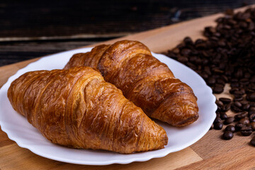 Croissants on a white plate and coffee beans on a wooden board