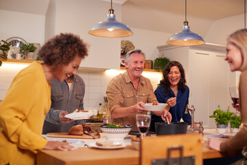 Group Of Mature Friends Meeting At Home Serving Food At Dinner Party And Drinking Wine Together