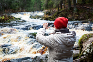 Traveller makes photo on smartphone in forest with karelian waterfalls.