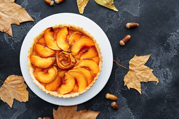 Top view of an apple pie on black background with dry leaves