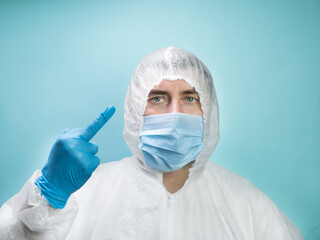 Man in medical mask wearing protective uniform on blue background show middle finger
