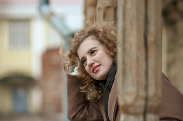 Portrait of a smiling young woman with curly hair on the porch of an old wooden house. Outside.