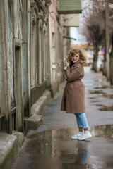 Fototapeta premium A beautiful young woman walks down the street with wet asphalt. The girl turns back