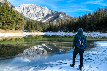 A man walking around the shore of Green Lake, Austria. Powder snow covering the mountains and ground. Soft reflections of Alps in calm lake's water. Winter landscape of Austrian Alps. Calmness
