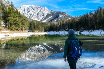 A man walking around the shore of Green Lake, Austria. Powder snow covering the mountains and ground. Soft reflections of Alps in calm lake's water. Winter landscape of Austrian Alps. Calmness