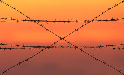 The rising sun and the crimson sky are crossed by several strands of barbed wire. It looks unusual and ominous.