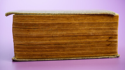 An old closed book lies on a pink background.