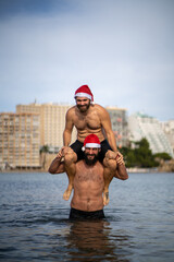 Fototapeta na wymiar Two friends with Santa Claus hat playing holding one to each other at the beach in Mallorca