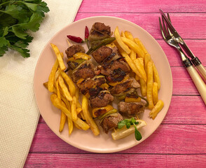 Spicy grilled pork skewers with bacon, chili pepper, bell pepper, onions and french fries. 