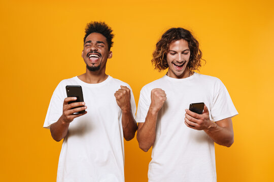 Excited multicultural guys using smartphones and making winner gesture