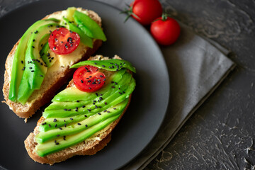 Fresh sandwich on dark rye bread made with fresh sliced avocados, cheese and cherry tomatoes. Top view
