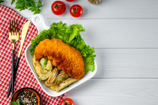 Pork schnitzel with baked potatoes on white wooden background top view, free space for text