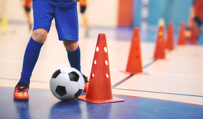 Football futsal training for children. Soccer training dribbling cone drill. Indoor soccer young player with a soccer ball in a sports hall. Player in blue uniform. Sport background