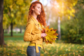 Cute redhaired woman holding autumn leafs in the natur