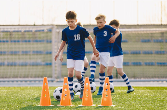 Young boys playing football training game. Happy children kicking soccer balls on practice pitch. Soccer training stadium in the background. School age boys in soccer blue jersey shirts