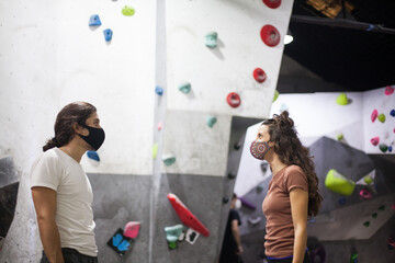 young fit woman and man climbers wearing mask on steep rock wall indoors