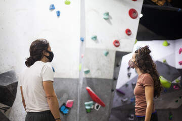 young fit woman and man climbers wearing mask on steep rock wall indoors