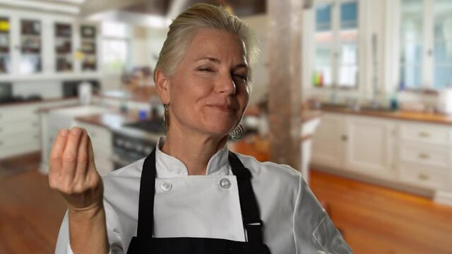 Portrait of happy and smiling professional chef woman giving a chef’s kiss in a kitchen.