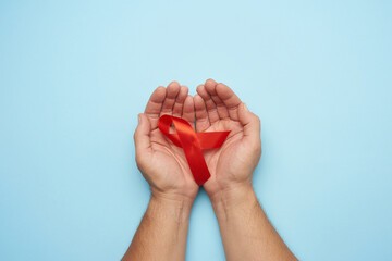 male hands holds a red ribbon - a symbol of the fight against disease AIDS