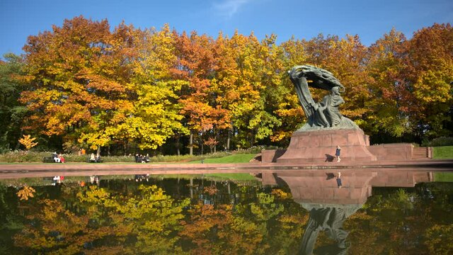 WARSAW, POLAND - OCTOBER 25, 2020: People relaxing at the Frederic Chopin monument in the Lazienki Park in Warsaw during autumn afternoon. Monument was designed by Waclaw Szymanowski and Oskar Sosnows