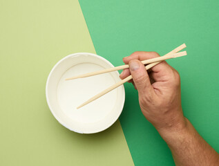 Pair of wooden chopsticks in a male hand and empty paper plate on a green background