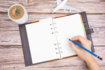 hand of women holding pencil and writting diary on wooden table with cactus and plane model