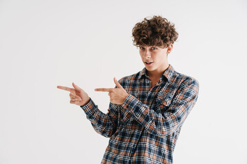 Pleased curly guy looking at camera and pointing fingers aside
