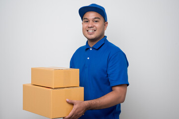 Young smiling asian delivery man in blue uniform holding box parcel cardboard on isolated white background.