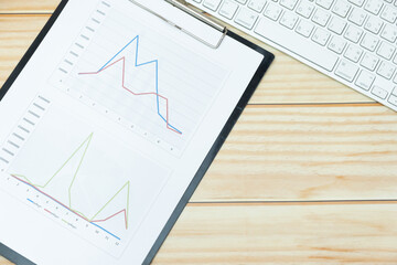 graph on paper sheet and computer keyboard on wooden desk in business concept