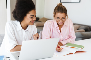 Joyful multicultural students girls doing homework with laptop