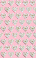 Valentine's day layout. repeating heart pattern of white hydrangea flowers on a pink background. vertical frame, flat lay, top view