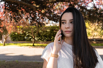 Young black-haired woman talking on the phone. Background with autumn vegetation.