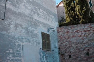 Isolated green window in a ruined wall of a building near a medieval brick wall (Corinaldo, Marche, Italy)