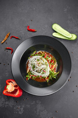 Vegetable salad with arugula, bell pepper, cucumber and flax seeds, on a black background
