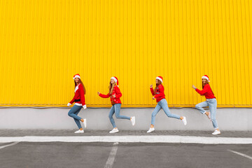Group of happy excited friends in santa claus hats having fun and jumping against yellow wall