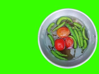 closeup of tomatoes and green chili peppers in a bowl isolated on green background
