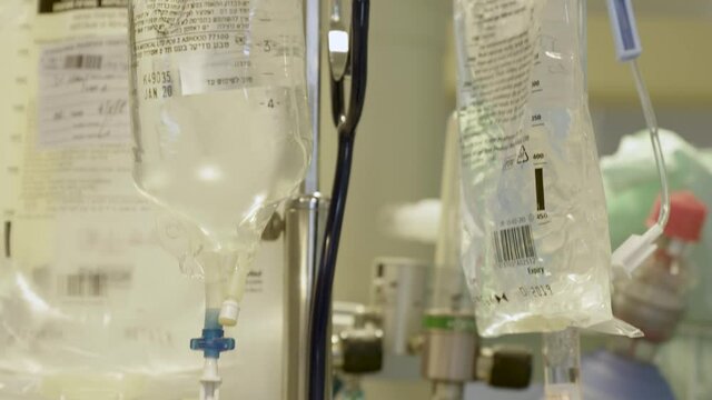 Several Intravenous Fluid Bags Hanging On The Intravenous Pole Next To Oxygen Tank In A Patient's Room In The Hospital. - tilt down shot