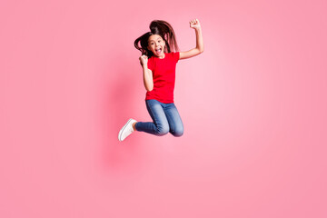 Full body photo of ecstatic kid girl jump raise fists wear red t-shirt jeans isolated over pastel color background