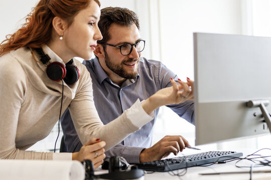 Two office workers discuss about a new project at the office. They looking a the computer screen.	
