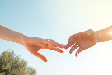 two hands with wedding rings against a blue clear sky are reaching out to each other..