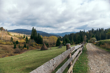 Fototapeta na wymiar Beautiful autumn landscape of the Carpathian village in the mountains and a path along the fence. haystacks and coniferous forest