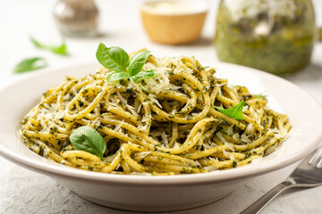 Spaghetti pasta with pesto sauce, parmesan cheese and basil leaves in plate on concrete background