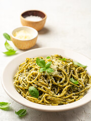 Spaghetti pasta with pesto sauce, parmesan cheese and basil leaves in plate on concrete background